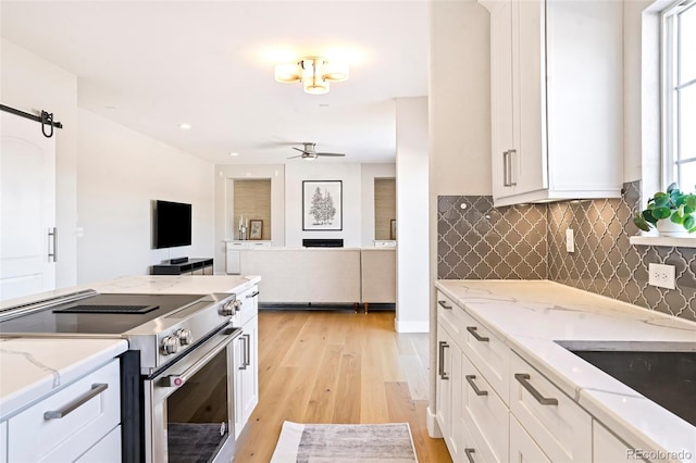 kitchen featuring stainless steel stove, white cabinets, ceiling fan, a barn door, and light wood-type flooring