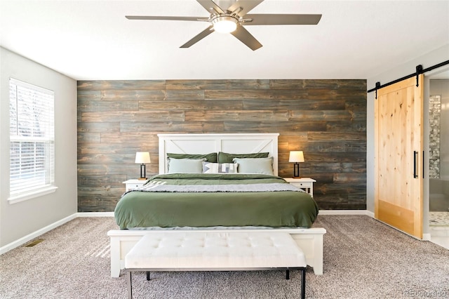 carpeted bedroom with multiple windows, ceiling fan, a barn door, and wooden walls