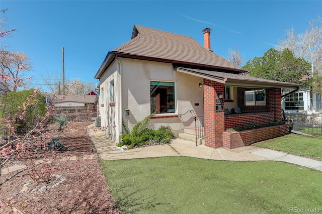 view of front of house featuring stucco siding, a chimney, a front yard, a shingled roof, and covered porch