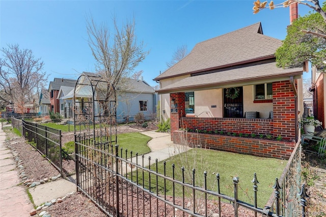 view of front facade with stucco siding, a front lawn, brick siding, fence, and a shingled roof