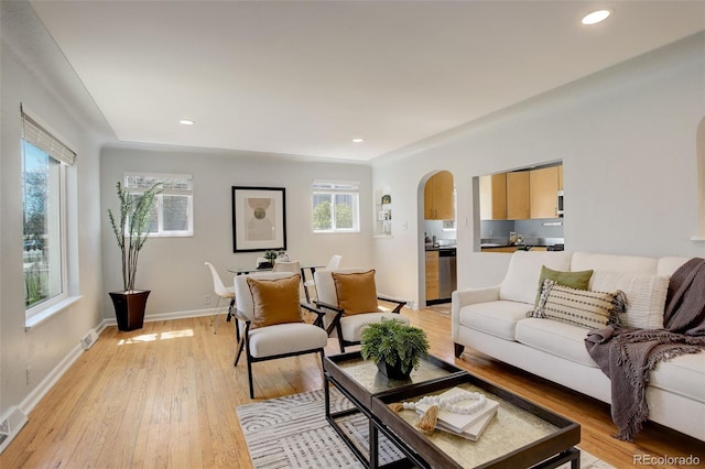 living room featuring a wealth of natural light, arched walkways, light wood-style floors, and baseboards