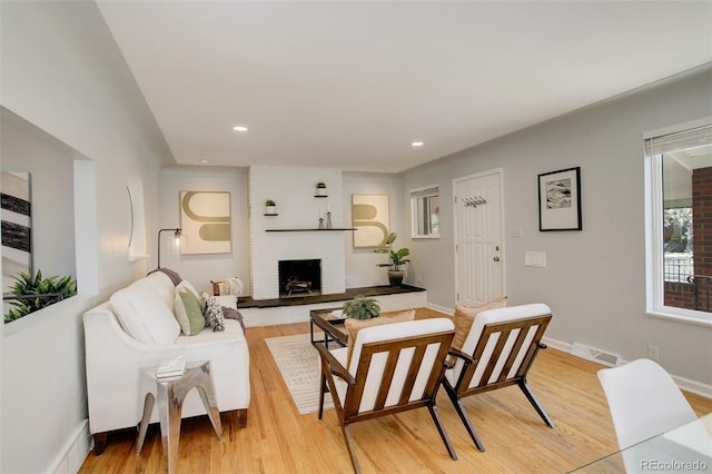 living room featuring light wood-type flooring, a brick fireplace, visible vents, and recessed lighting