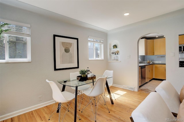 dining room with arched walkways, light wood finished floors, baseboards, and visible vents