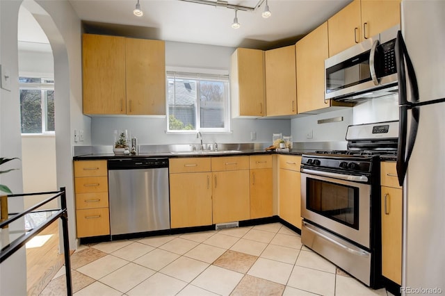 kitchen featuring a sink, appliances with stainless steel finishes, arched walkways, and light brown cabinets