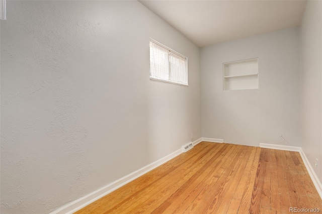 spare room with light wood-style floors, baseboards, built in features, and visible vents