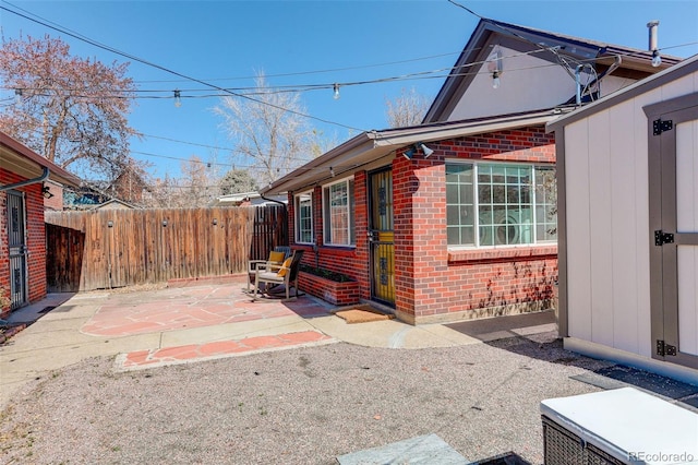 view of property exterior featuring a patio, fence, and brick siding