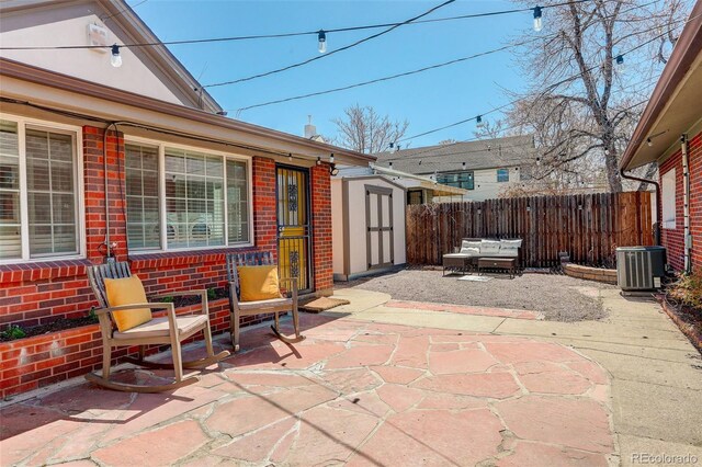 view of patio / terrace featuring a shed, central AC unit, fence, and an outbuilding