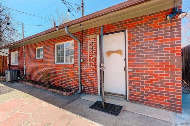 entrance to property with fence, central AC unit, and brick siding