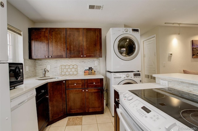 kitchen with white appliances, light countertops, stacked washer / dryer, visible vents, and a sink