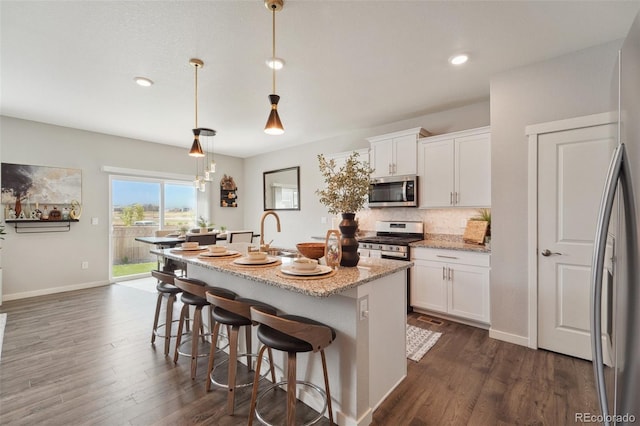 kitchen with stainless steel appliances, white cabinetry, a center island with sink, and hanging light fixtures