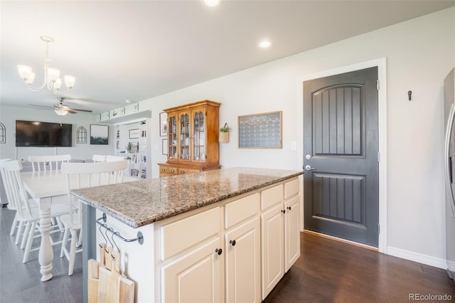 kitchen featuring dark hardwood / wood-style floors, ceiling fan with notable chandelier, a kitchen island, decorative light fixtures, and light stone countertops