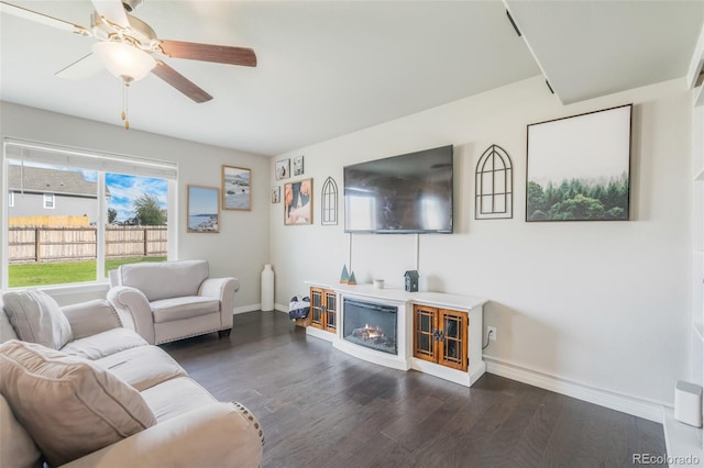 living room with ceiling fan, a fireplace, and dark wood-type flooring