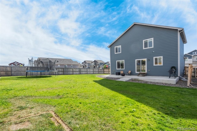 rear view of property featuring a trampoline, a patio area, and a yard