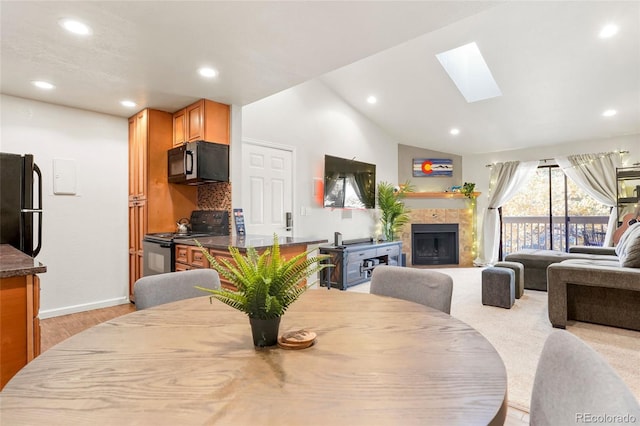 dining room featuring lofted ceiling with skylight, a tile fireplace, and light hardwood / wood-style floors