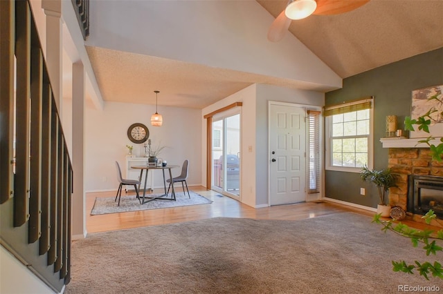 entryway with a stone fireplace, light hardwood / wood-style flooring, vaulted ceiling, a textured ceiling, and ceiling fan