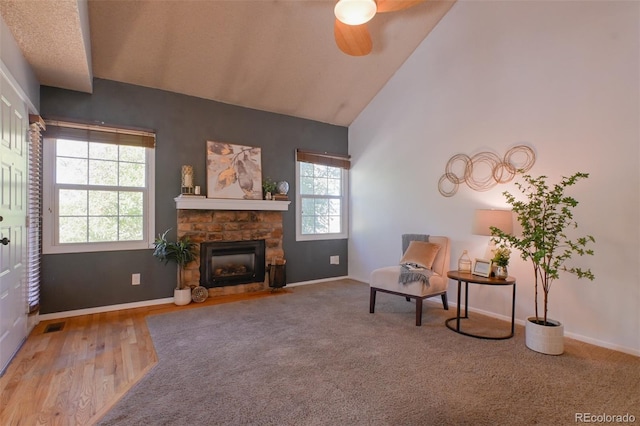 living area with ceiling fan, a stone fireplace, a wealth of natural light, and hardwood / wood-style floors