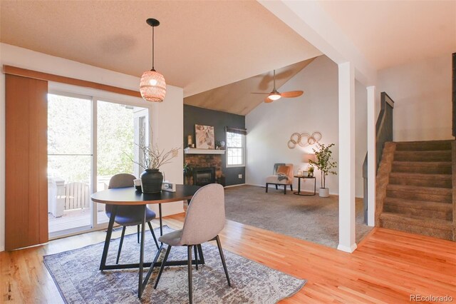 dining space with ceiling fan, a stone fireplace, wood-type flooring, and lofted ceiling