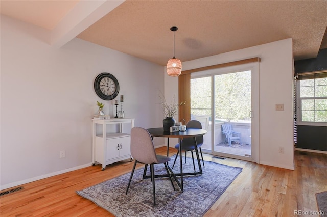 dining area with beamed ceiling, hardwood / wood-style floors, and a textured ceiling