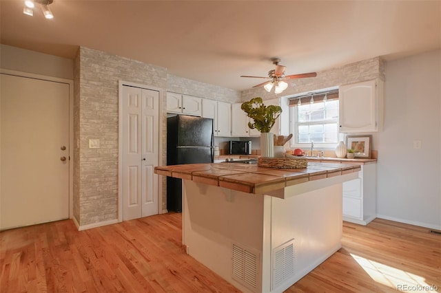 kitchen with black fridge, ceiling fan, white cabinetry, light wood-type flooring, and tile counters