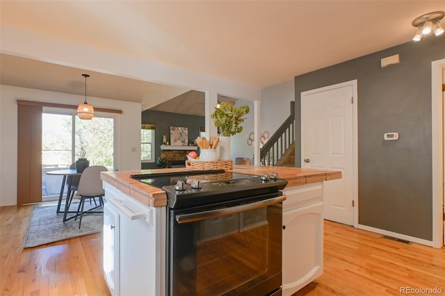 kitchen with white cabinets, black / electric stove, hanging light fixtures, and light wood-type flooring