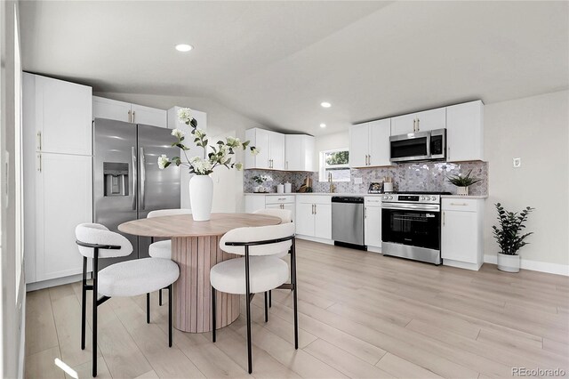 8497 Madison Way, Denver, CO 80229 - kitchen featuring appliances with stainless steel finishes, vaulted ceiling, tasteful backsplash, light wood-style floors, and white cabinetry