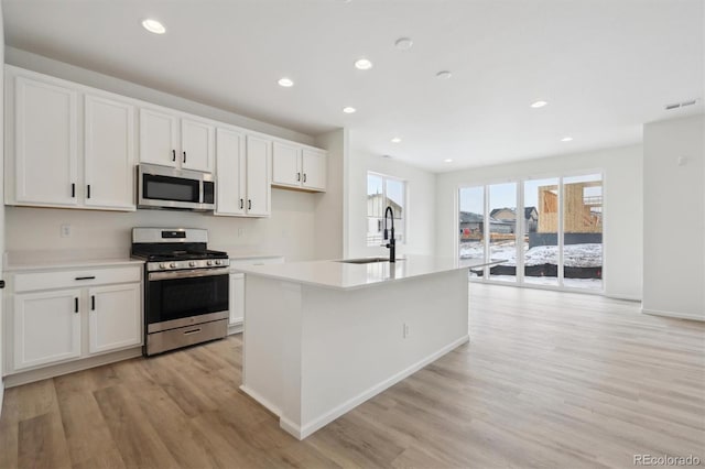 kitchen featuring appliances with stainless steel finishes, white cabinets, light countertops, and an island with sink