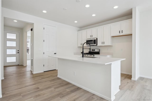 kitchen featuring stainless steel appliances, white cabinetry, light wood-style floors, light countertops, and an island with sink