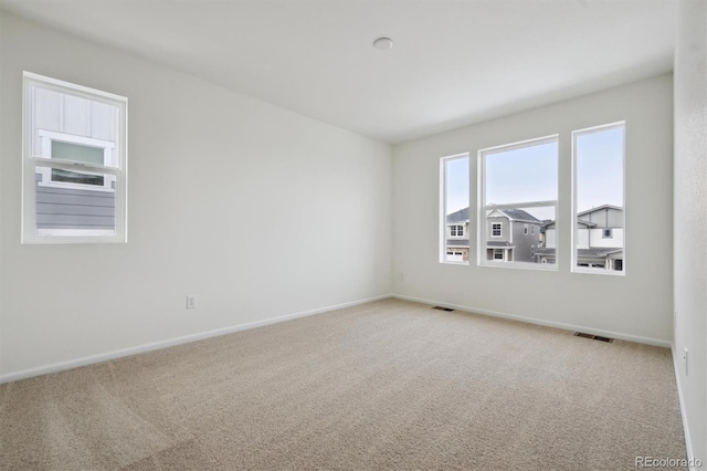 empty room featuring baseboards, visible vents, and light colored carpet