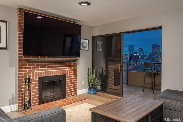 living area with baseboards, a brick fireplace, and wood finished floors