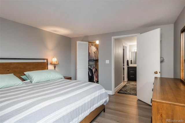 bedroom with a spacious closet, wood finished floors, baseboards, and a closet