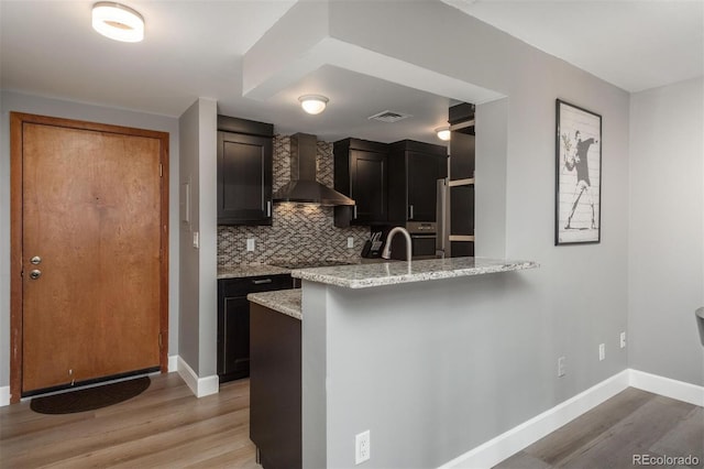 kitchen with wall chimney exhaust hood, light stone countertops, light wood-type flooring, and backsplash