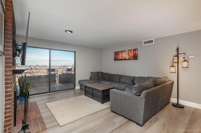 living room featuring visible vents, baseboards, a brick fireplace, and wood finished floors