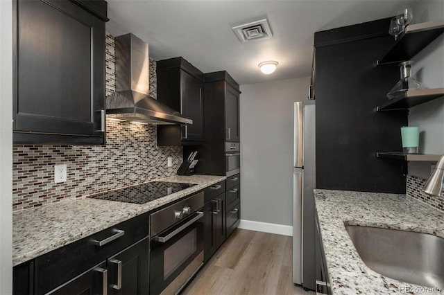 kitchen with wall chimney exhaust hood, light wood-type flooring, open shelves, a sink, and stainless steel appliances