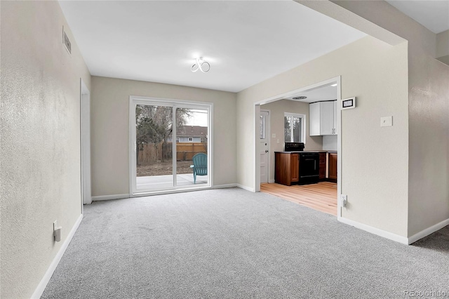 unfurnished living room featuring light carpet, a textured wall, visible vents, and baseboards