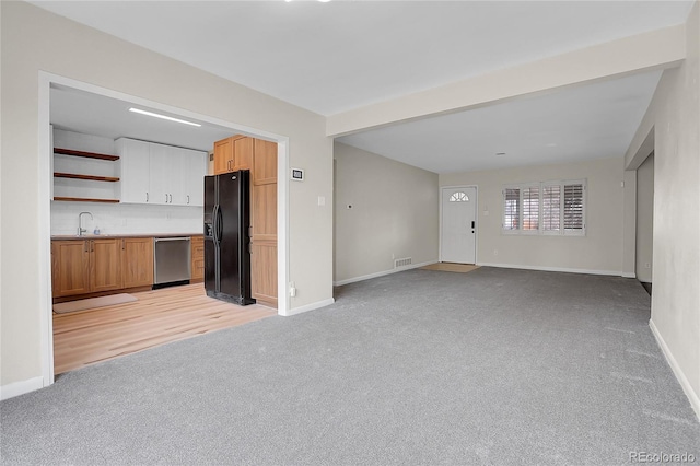 unfurnished living room with baseboards, a sink, visible vents, and light colored carpet