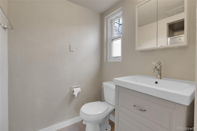 bathroom with toilet, a textured wall, baseboards, and vanity