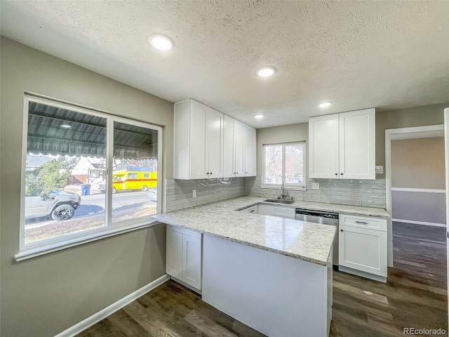 kitchen with dishwasher, white cabinetry, light stone countertops, dark hardwood / wood-style flooring, and kitchen peninsula