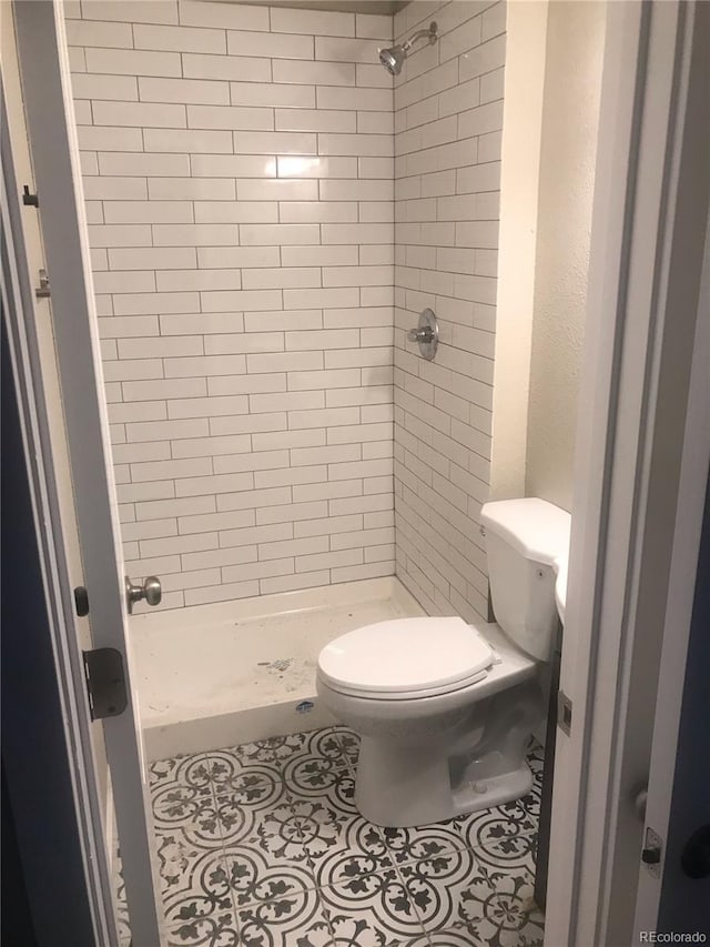 bathroom featuring a tile shower, tile patterned floors, and toilet