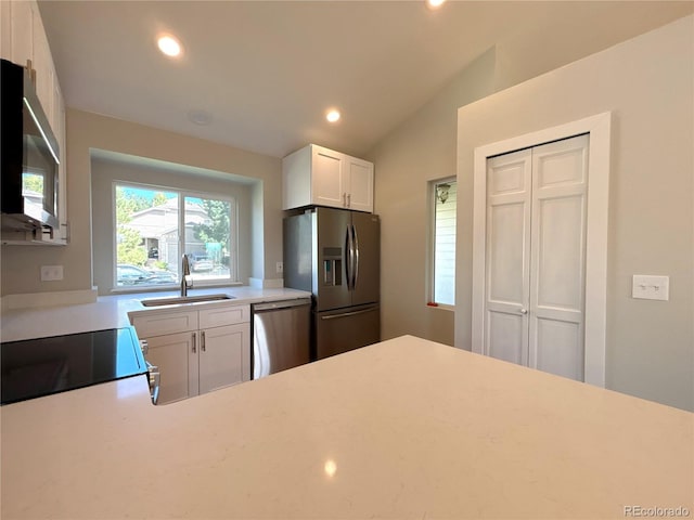 kitchen with stainless steel appliances, vaulted ceiling, white cabinetry, and sink