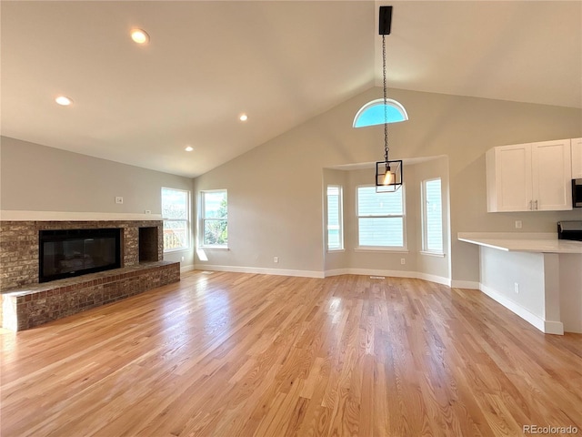 unfurnished living room featuring a brick fireplace, light hardwood / wood-style flooring, and lofted ceiling