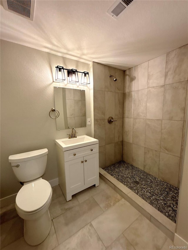 bathroom featuring a tile shower, tile patterned flooring, vanity, and toilet