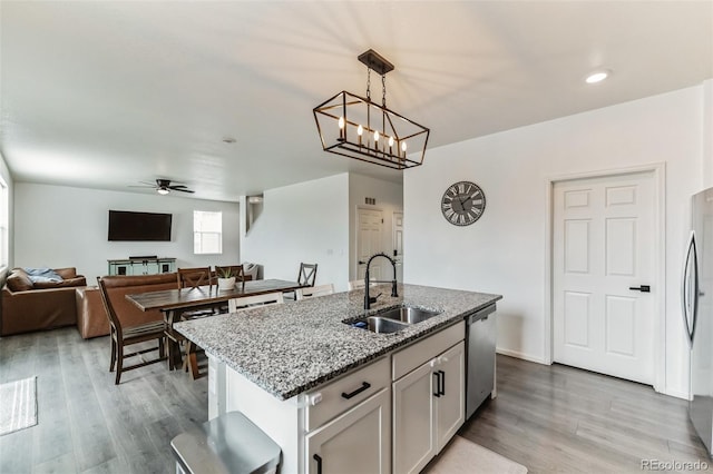 kitchen featuring light wood-style flooring, appliances with stainless steel finishes, open floor plan, a sink, and ceiling fan with notable chandelier