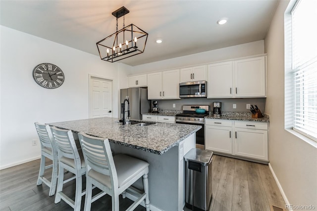 kitchen featuring appliances with stainless steel finishes, a sink, a kitchen island with sink, and white cabinetry