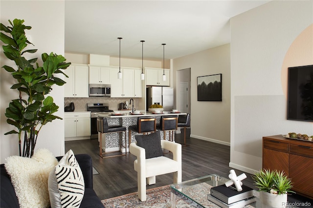kitchen with decorative backsplash, an island with sink, dark wood finished floors, and appliances with stainless steel finishes