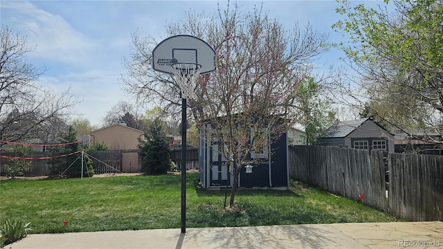 view of sport court with a lawn, a fenced backyard, and a storage unit