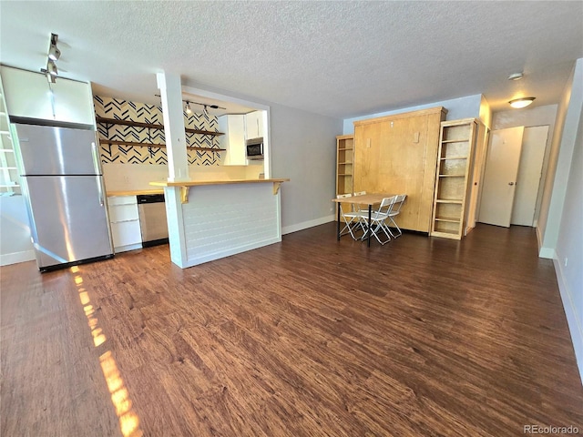 kitchen with dark wood-type flooring, a kitchen breakfast bar, a textured ceiling, appliances with stainless steel finishes, and kitchen peninsula