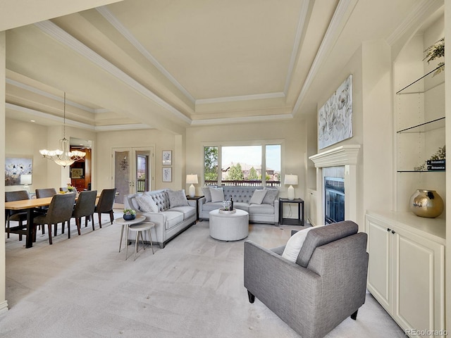 living area with a tray ceiling, a chandelier, ornamental molding, a glass covered fireplace, and light colored carpet