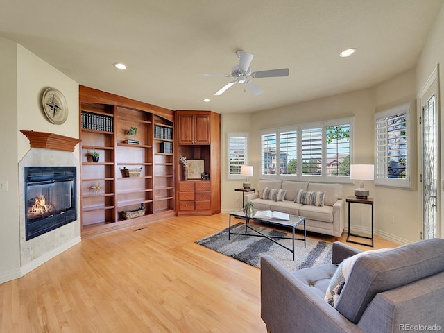 living room with ceiling fan, a glass covered fireplace, recessed lighting, light wood-style flooring, and baseboards