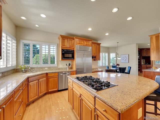 kitchen with stainless steel appliances, recessed lighting, a kitchen bar, light wood finished floors, and light stone countertops