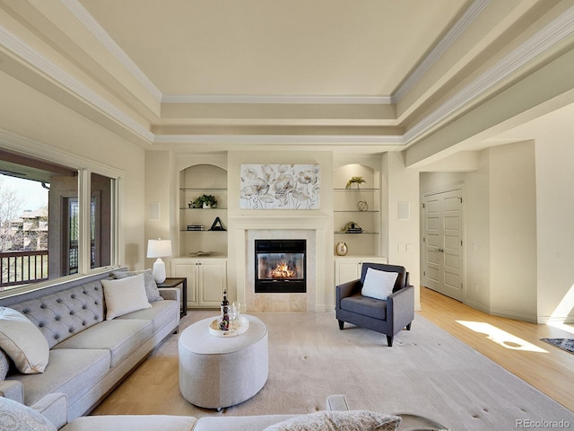living area featuring a glass covered fireplace, built in shelves, crown molding, baseboards, and a raised ceiling